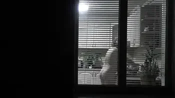 Peeping. Voyeur. Neighbor pervert voyeur in evening on street looks out window as naked sexy neighbor in kitchen prepares dinner for her husband. Naked in public. Naked at home. Family.  Outdoor